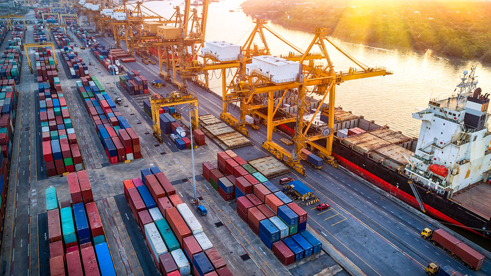 Colorful cargo for shipping and transportation on a dock at sunset next to a body of water with ships in the port