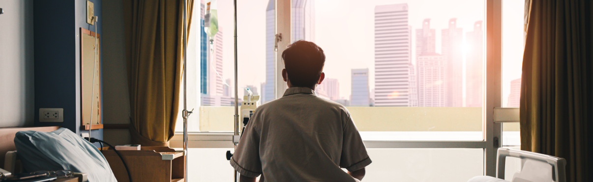 Patient sitting on edge of bed, looking out of the window.