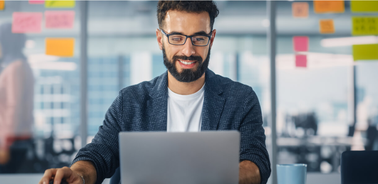 Male developer smiling and working at laptop in office.