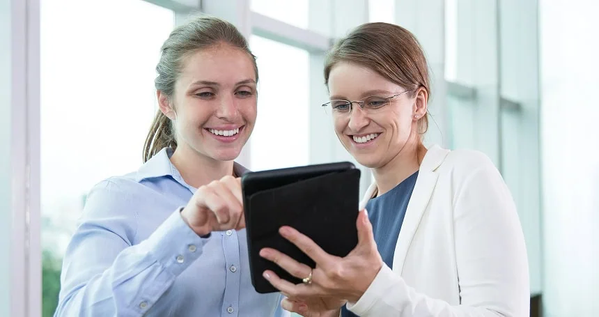 Two healthcare professionals smiling while reviewing information on a tablet together